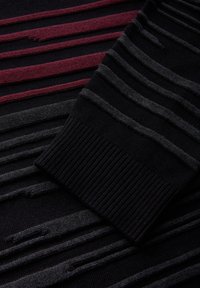 Tissu en maille noire avec des rayures horizontales en relief en gris foncé et rouge foncé, montrant un détail de poignet côtelé.