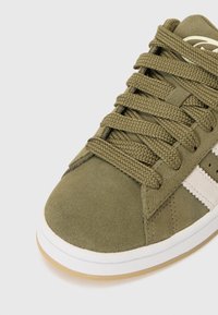 Baskets en nubuck vert olive avec une surface texturée, dotées de bandes latérales blanches, de lacets épais assortis et d'une semelle en caoutchouc gomme contrastante.