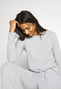 Ljust grå, strukturerad stickad loungewear-set med ett ribbat mönster. Långärmad topp och lösa byxor med dragsko i midjan och raka ben.
