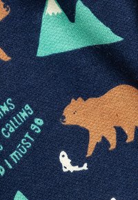 La tela de color azul marino presenta ilustraciones de un oso pardo y peces blancos, con patrones de montañas verdes y texto en un tono verde azulado claro, mostrando un diseño juguetón.