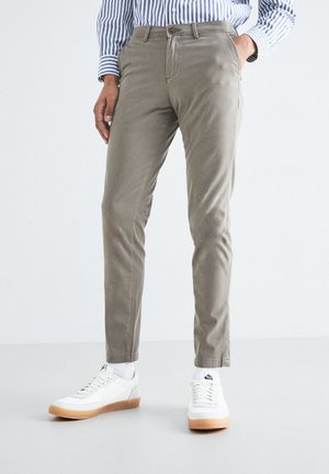 Pantaloni grigi chiari realizzati in tessuto misto cotone, con vestibilità slim, tasche laterali e chiusura con bottone, abbinati a sneakers bianche su uno sfondo neutro.