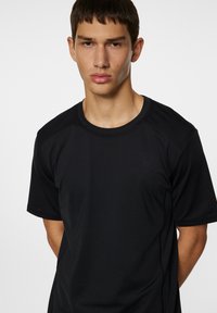 Svart kortärmad träningströja i ett mjukt, fukttransporterande material. Har en rund halsringning och en diskret logotyp på bröstet.