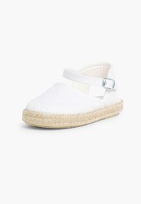 Zapato espadrille blanco con parte superior texturizada, correa en el tobillo y suela de yute. Presenta una punta redondeada y un detalle cosido alrededor del borde.