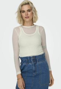 Un top alb cu mânecă lungă, cu dungi, suprapus peste un pulover de mână lungă, transparent, cu dungi. Asortat cu o fustă din denim, cu talie înaltă, care are buzunare frontale.