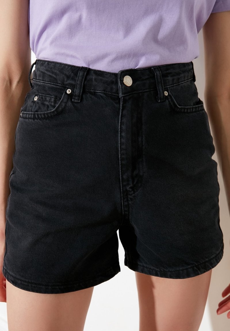 Pantalones cortos de mezclilla negros de cintura alta, con diseño de cinco bolsillos y herrajes plateados. Presentan una textura suave y un corte recto.