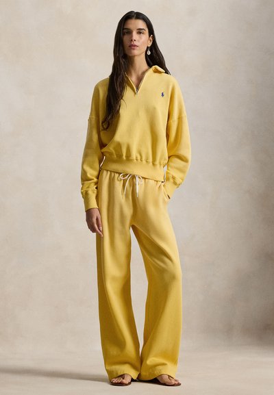 Κίτρινο φούτερ με φανέλα βαμβακερού μίγματος και φερμουάρ στον λαιμό, συνδυασμένο με παντελόνι φαρδύ με ελαστική μέση και κορδόνι. Διαθέτει μαλακή υφή.