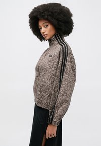 Καφέ μπουφάν με σχέδιο καμηλοπάρδαλης, ψηλό γιακά και μαύρες ρίγες κατά μήκος των μανικιών. Διαθέτει ελαστικές μανσέτες και τελείωμα για εφαρμοστή εμφάνιση.