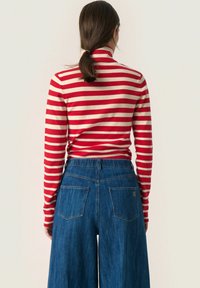 Rdeče in smetankovo bele črtaste dolge rokave turtleneck bluze, kombinirane z modrimi širokima jeans hlačami, ki imajo zadnje žepke in visok pas.