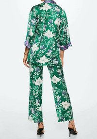 Completo in due pezzi a stampa floreale verde realizzato in satin leggero, con una blusa ampia a maniche ¾ e pantaloni a gamba larga.