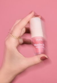 Pupa Wonder Me Shake Blush en un frasco transparente con tapa blanca, mostrando un líquido rosa. Mano sosteniendo el frasco con acabado mate.