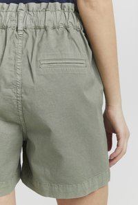 Zelené bavlněné šortky s elastickým pasem, zadní kapsou na patch a uvolněným střihem. Hladká textura a volnočasový design.