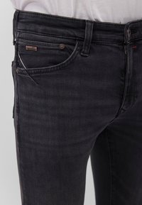 Black denim jeans with a slim fit, featuring a classic five-pocket design, metal button closure, and subtle branding on the front pocket.