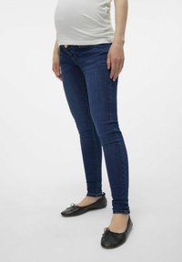 Jeans de mezclilla azul ajustados con una cintura de altura media. Llevados con bailarinas negras. La tela tiene una textura suave y un ligero estiramiento.