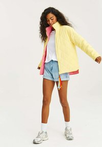 Žlutá prošívaná bunda s růžovým vnitřkem, vysokým límcem a zipem. Vytvořeno s denimovými šortkami a bílými ponožkami, nošeno s stříbrnými teniskami.