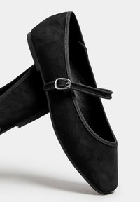 Bailarinas de ante negro con puntera redondeada, suela plana y una correa decorativa con un acento de hebilla plateada.