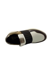 Zapatilla de piel blanca con una correa negra texturizada que presenta remaches, acentos marrones y puntera redonda. Revestimiento interior suave y suela acolchada.