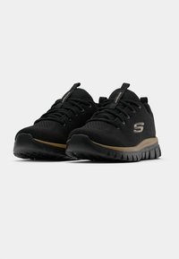 Schwarze Sportschuhe mit Mesh-Obermaterial, strukturierten Schnürsenkeln und einem goldenen Akzentstreifen. Verfügt über eine profilierten, flexiblen Sohle für Grip und Unterstützung.