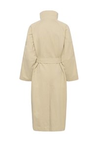 Smėlio spalvos paltas iki kelių su plačiomis rankovėmis, aukšta apykakle ir pritvirtintu diržu, matomas nugara baltoje fone.