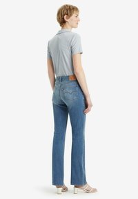 Vaqueros de pierna recta azul claro con cintura alta, con bolsillos traseros y una etiqueta de cuero. Combinados con una camiseta polo de manga corta gris claro.