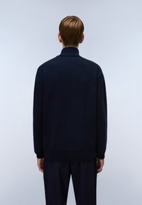 Marinblå stickad tröja med hög krage, ribbade muddar och nederkant samt en slät textur. Tröjan är designad för en avslappnad passform.