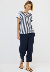 Blusa a maniche corte a righe blu e bianche, vestibilità rilassata, design a scollo a V. Abbinata a pantaloni blu a 3/4 e sandali marrone chiaro.