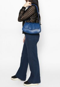 Borsa a mano in pelle blu con una texture liscia, parte superiore curva e tracolla regolabile. Abbinata a jeans a zampa d'elefante blu navy e a un top a righe nere.