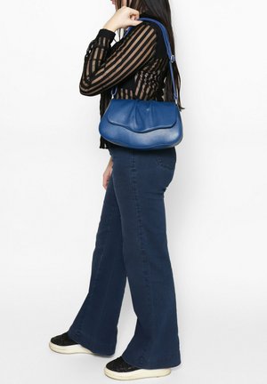 Blaue Lederhandtasche mit glatter Textur, gebogenem Oberteil und verstellbarem Tragegurt. Kombiniert mit navyblauen Schlagjeans und einem schwarz gestreiften Oberteil.