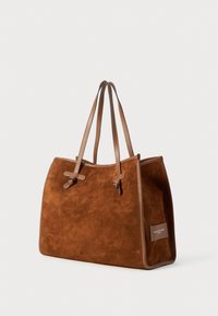 Sac fourre-tout en daim marron avec deux poignées en cuir, détails noués, forme structuré et une petite étiquette de logo sur un côté.