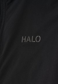 Schwarzer Stoff mit einer genähten Naht und dem reflektierenden "HALO"-Logo, das im mittleren rechten Bereich aufgedruckt ist.