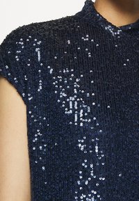 Navy sequin top with a textured surface, featuring a high neckline and short sleeves, showcasing reflective details and a shimmering finish.