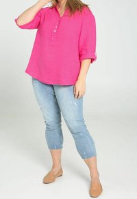 Chemise en lin fuchsia à trois boutons, manches retroussées, associée à un jean court bleu clair déchiré et des chaussures plates beige.