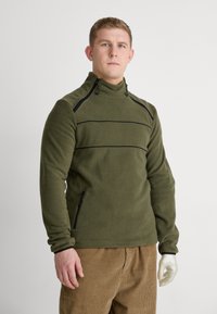 Olivově zelený fleece svetr s vysokým límcem, černými zipovými detaily a bočními kapsami. Měkká textura s horizontálním černým pruhovým detailem.