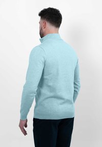 Lichtblauwe gebreide trui met hoge kraag, voorzien van lange mouwen en een ribbelzoom. De stof lijkt zacht en lichtjes gestructureerd.