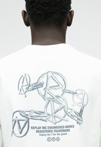 Λευκή μπλούζα με κουκούλα που διαθέτει γκρι γραφικό σχέδιο στο πίσω μέρος, συμπεριλαμβανομένων διασυνδεδεμένων σχημάτων και κειμένου: "REPLAY INC ENGINEERED WORKS."