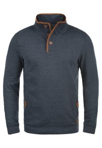 Marineblauwe pullover met een hoge kraag, bruine accenten op de kraag en knopen, en een gestructureerde stof. Voorzien van zijzakken en geribbelde manchetten.