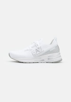 White athletic sneaker with knit upper, lace closure, and thick cushioned sole labeled "EA7 Emporio Armani" and "Crusher" on the side.
