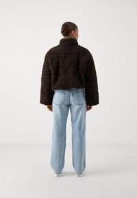 Chundelatá hnědá oversize bunda s vysokým límcem, kombinovaná s světle modrými širokými džíny. Disponuje texturovanou tkaninou a volným střihem.