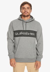 Grijze hoodie van zachte stof, met een zwarte horizontale streep en witte tekst "Quiksilver," verstelbare trekkoordkap en kangoeroezak.