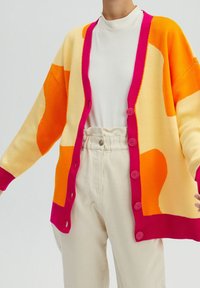 Kolorowy sweter kardigan wykonany na drutach w odcieniach pomarańczowego, żółtego i różowego, z zapięciem na guziki i ściągaczami przy mankietach. Lekki i o luźnym kroju.