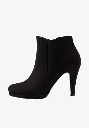 Botte noire à la cheville avec un bout pointu, un talon haut et une texture douce semblable à du daim. Elle se distingue par des panneaux élastiques sur les côtés et une silhouette lisse.
