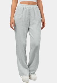 Lichtgrijze, ademende wijde broek in een gestructureerde stof met een elastische tailleband. Gestyled met witte sneakers.