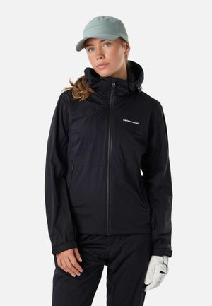 Femme portant une veste noire zippée, un pantalon noir, un gant blanc à la main droite et une casquette gris clair avec de longs cheveux bruns attachés.