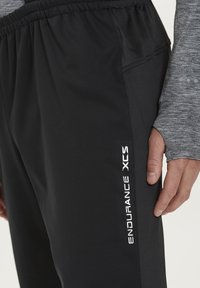 Sorte sportsbukser med elastisk talje og sidelommer. Funktioner hvid tekst "ENDURANCE XCS" langs venstre ben. Blødt, struktureret stof.