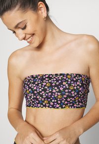 Top bandeau preto com um padrão colorido de flores e símbolos da paz, com acabamento amarelo nas bordas. Tecido suave com um design cropped.