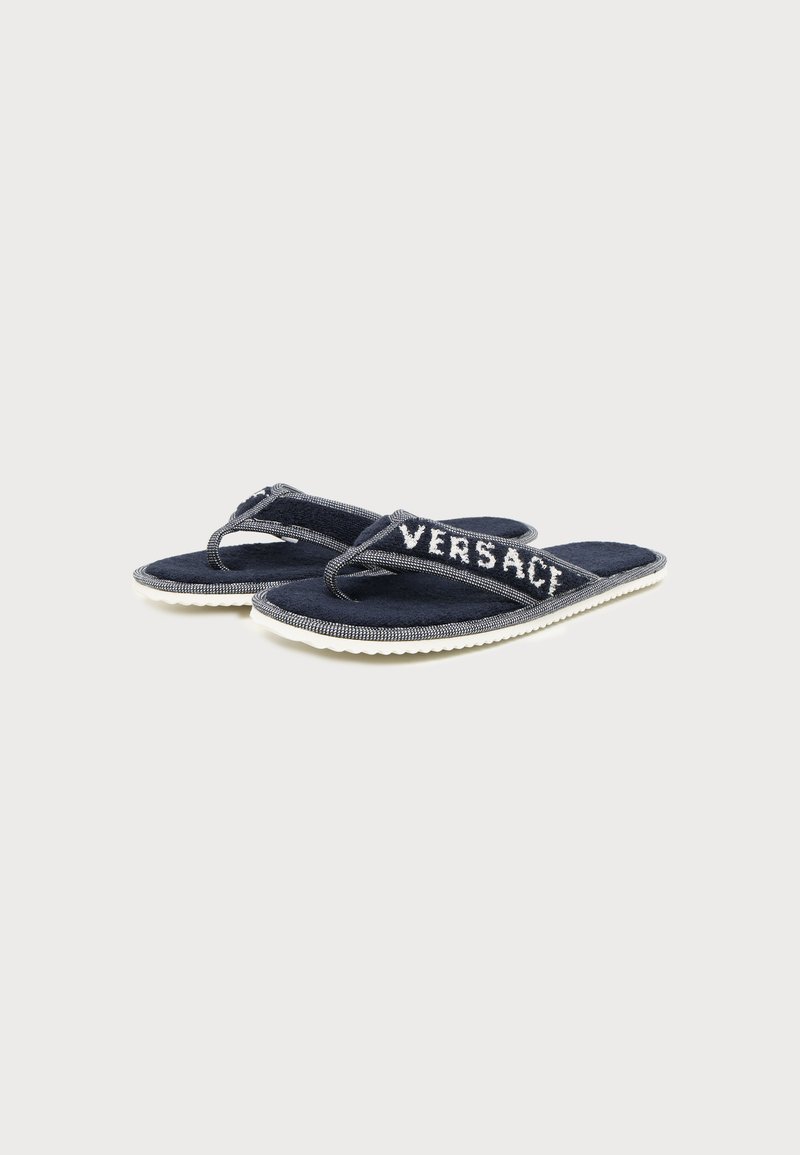 Pair of dark blue fabric flip-flops with white soles and "VERSACE" embroidered on the straps, displayed on a light background.