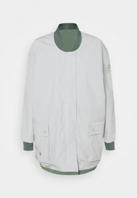 Jasnoszara kurtka bomberka z zielonym prążkowanym kołnierzem, mankietami i dolnym brzegiem, przednimi kieszeniami zapinanymi na zatrzaski oraz ukrytą zapięciem na zamek.