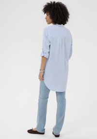 Heleroheline pikkade varrukatega särk, millel on kõver serv ja nööbitavad mansetid, kantud koos heleda teksade ja tumedate pruunide tasaste kingadega.