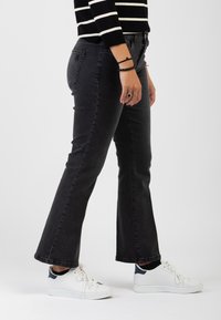 Jeans neri a campana con vita regolare, tasche laterali e design pulito, abbinati a sneakers bianche e una maglietta a righe in bianco e nero.