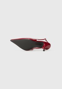 Chaussure à talon haut en cuir verni rouge avec un bout pointu, dotée d'un talon fin et d'une semelle extérieure noire texturée.