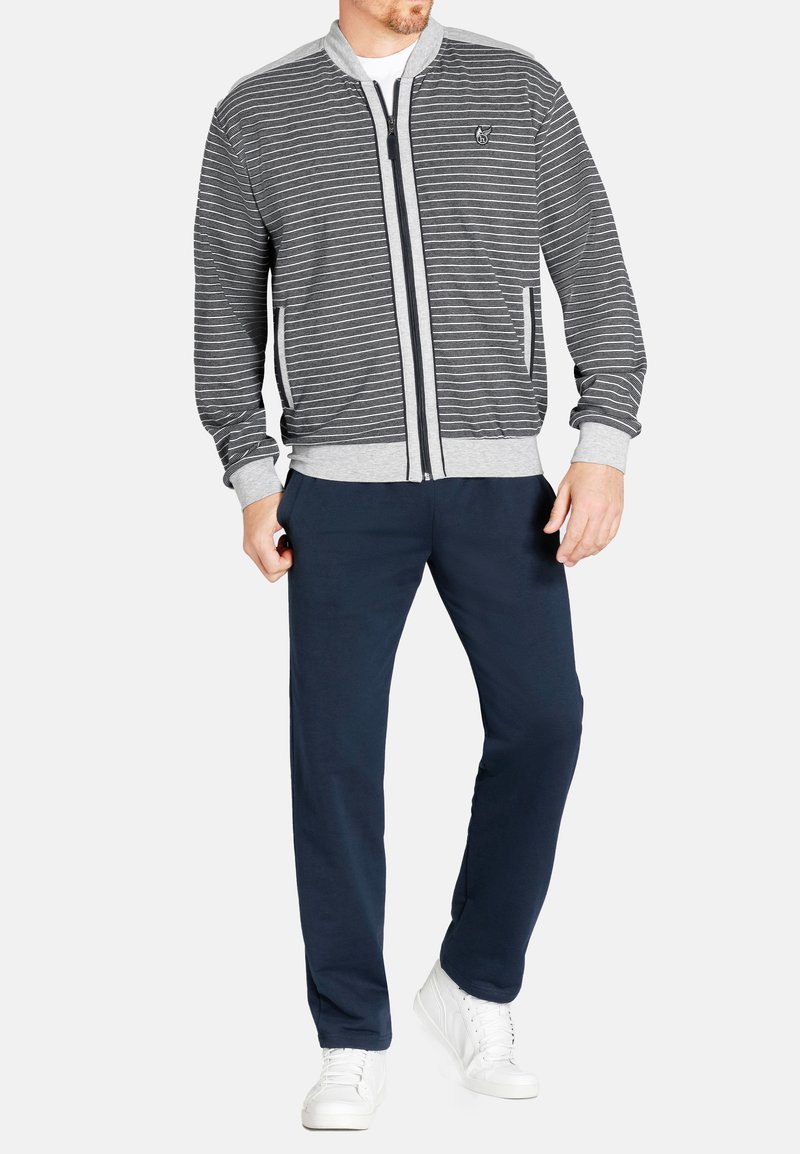 Grijze en witte gestreepte bomberjack met ribgebreide mouwen en kraag, gecombineerd met marineblauwe broek en witte sneakers. Voorzien van zijzakken en een logo.